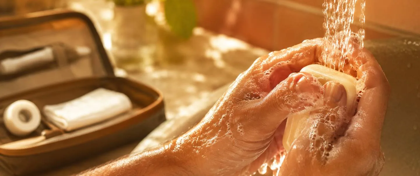 Manos lavándose con agua y jabón junto a un botiquín sencillo, en un baño luminoso