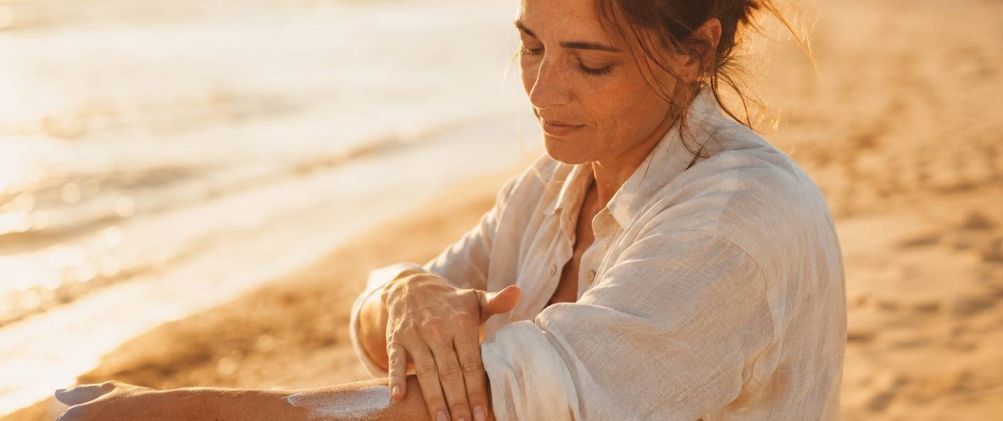 Mujer aplicándose protector solar en el brazo en la playa, con luz dorada de tarde