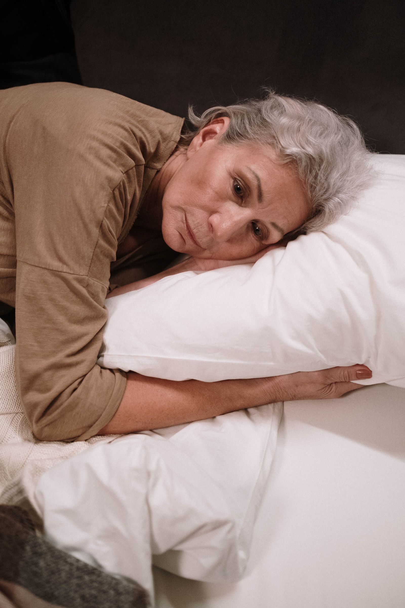 Mujer mayor descansando de lado sobre una almohada en su cama