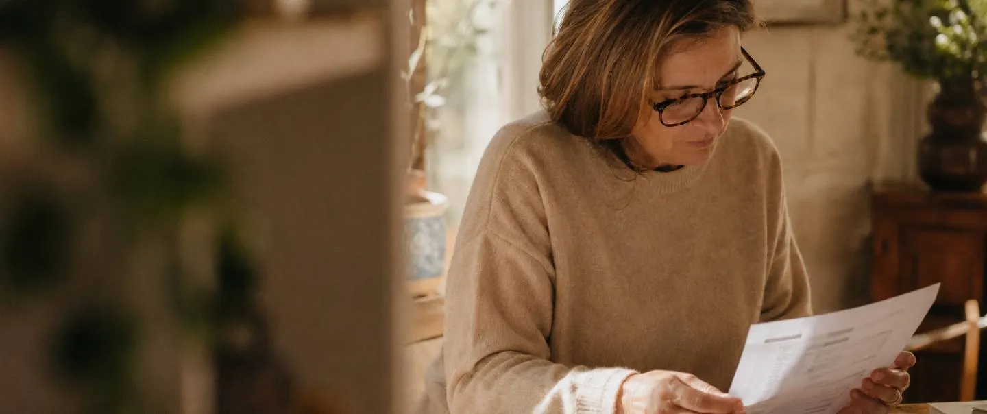 Mujer con gafas leyendo el informe de su analítica sentada a la mesa de casa
